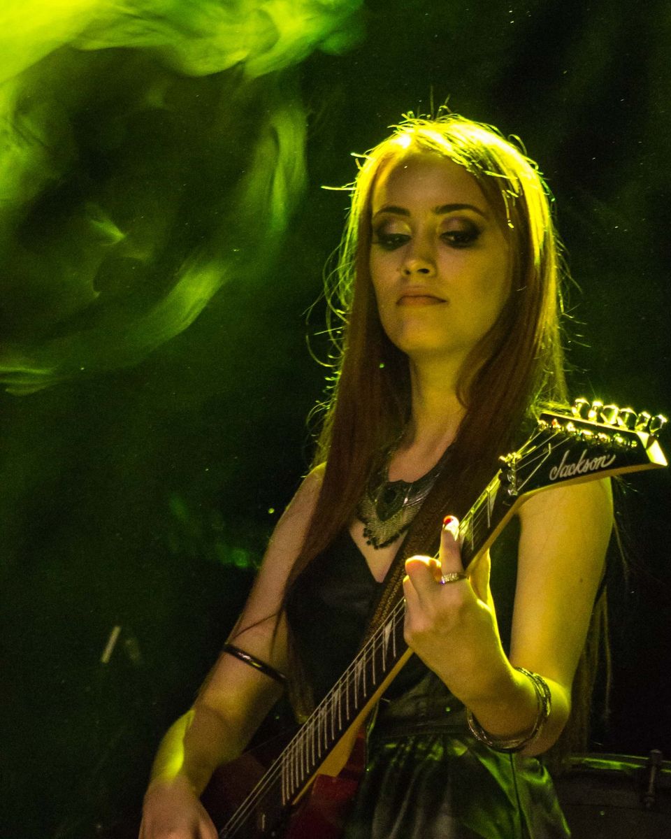 Kalina tocando guitarra elétrica em show, iluminada por fumaça verde.