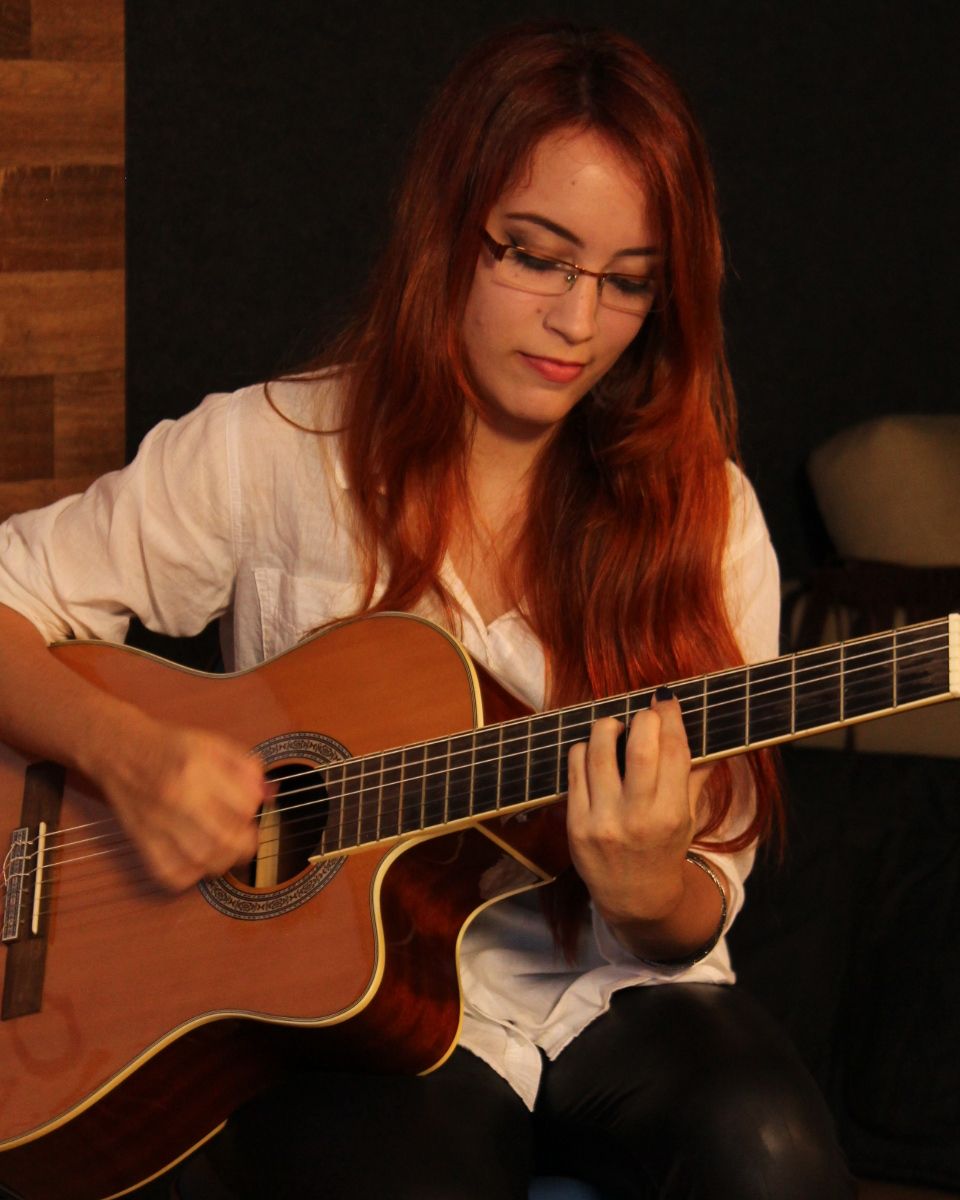 Kalina tocando violão sentada, em um estúdio.